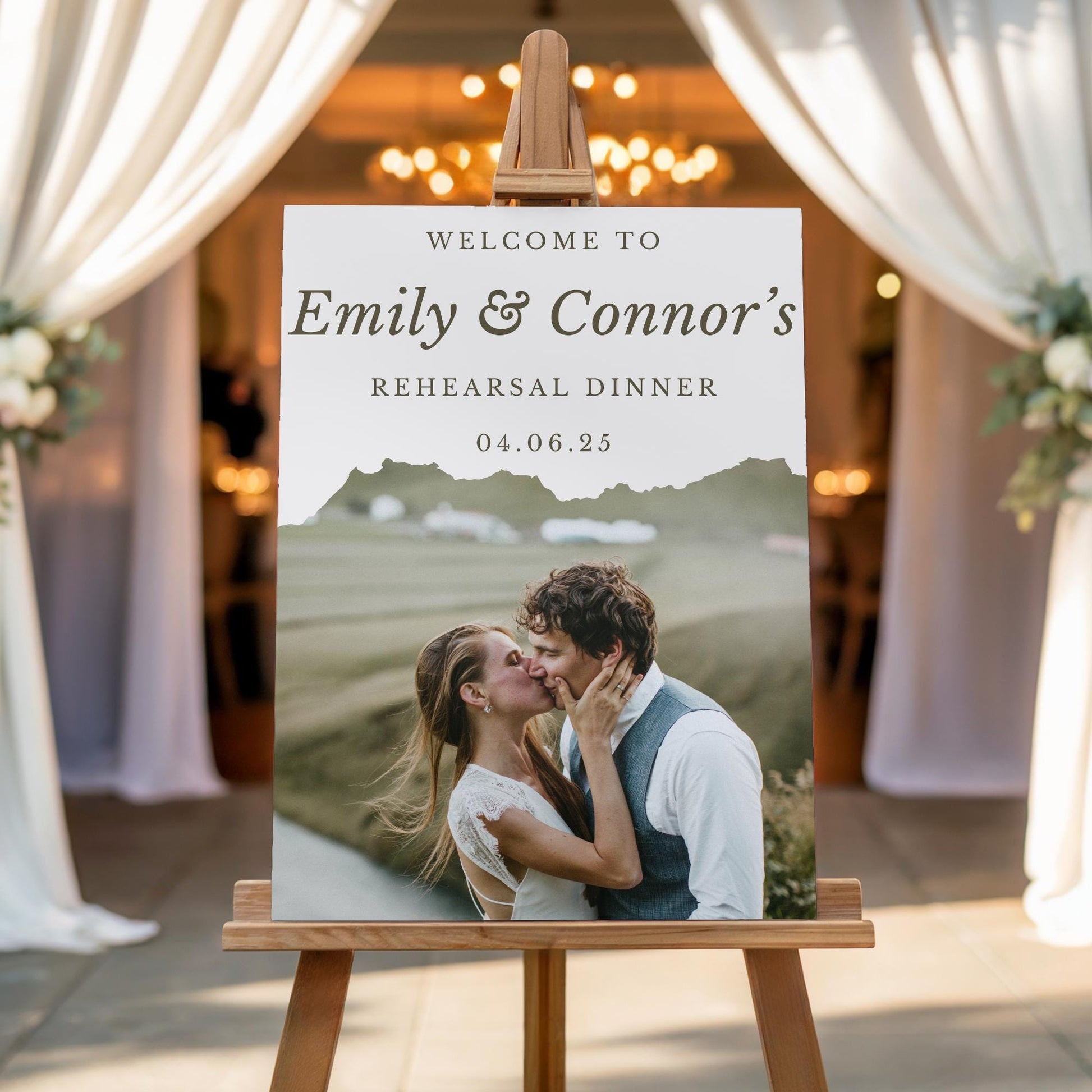 May include: Welcome to Emily & Connor's Rehearsal Dinner 04.06.25 sign with a photo of a couple kissing in front of a mountain range.